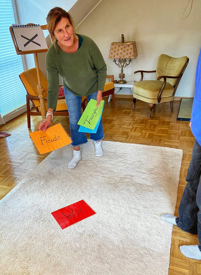 Johanna Bolwin, bei der Vorbereitung einer Kinesiologie Übung. Sie legt Zettel mit versch Wörter drauf "Wut", "Freude", "Traurigkeit", auf den Boden.